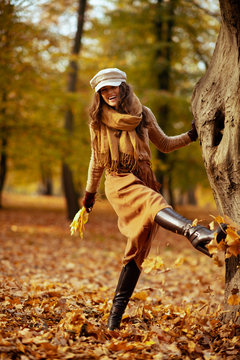modern woman outside in autumn park kicking leaves