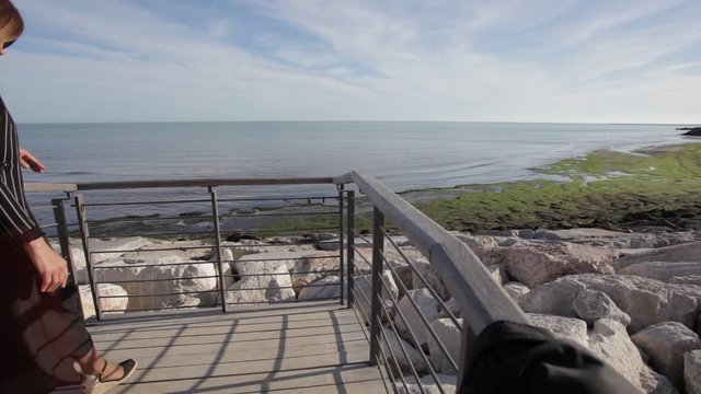 Woman with black elegant dress moved by the wind watching the sea on the horizon leaning against a railing. Concept: wanderlust, travel lifestyle. Caorle, Venice, Italy