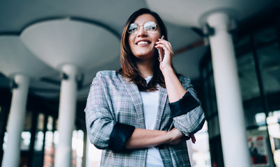Below view of millennial Turkish woman in eyewear for vision correction connecting to public wifi for making mobile call in roaming, happy female employee enjoying communication via smartphone