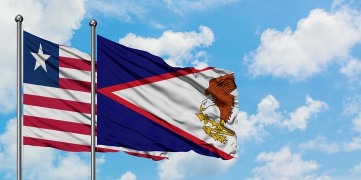 Liberia and American Samoa flag waving in the wind against white cloudy blue sky together. Diplomacy concept, international relations.