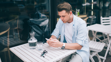 Stylish young man using phone at table