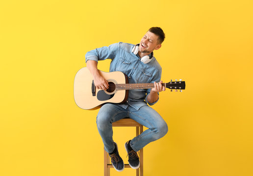 Handsome man playing guitar on color background