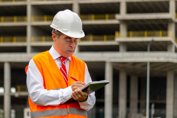 Fototapeta premium Construction engineer man in shirt and tie with safety helmet and vest works at construction site. Concept of people working in industrial field