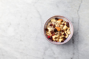 Bowl of granola with milk, nuts, raisins and cranberries. Concept for a tasty and healthy meal. Bright stone background. Top view. Copy space. 