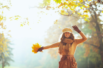 smiling trendy woman with yellow leaves outdoors in autumn park