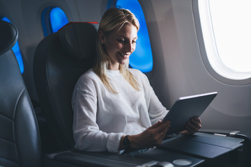 Happy carefree female passenger enjoying comfortable flight and Wifi internet connection on board.Caucasian young woman tourist shopping online airline website. Smiling blogger reading travel article