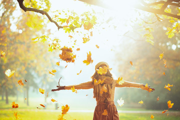 woman enjoying autumn and catching falling yellow leaves