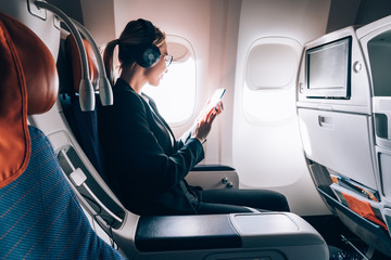 Caucasian female airplane passenger reading received email via mobile phone during trip connected...