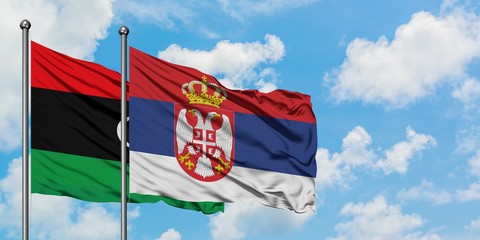 Libya and Serbia flag waving in the wind against white cloudy blue sky together. Diplomacy concept, international relations.