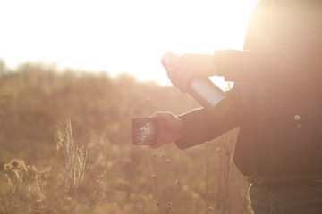 Fototapeta na wymiar A woman pours a hot drink from a thermos into a mug. Refreshment while hiking. Clink glasses of tea in the morning at dawn, three people drink tea. Metal cups on the nature. Hands warm hot coffee