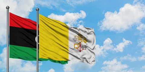 Libya and Vatican City flag waving in the wind against white cloudy blue sky together. Diplomacy concept, international relations.