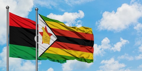 Libya and Zimbabwe flag waving in the wind against white cloudy blue sky together. Diplomacy concept, international relations.