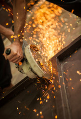 Worker cutting metal with grinder. Sparks while grinding iron. Selective low focus