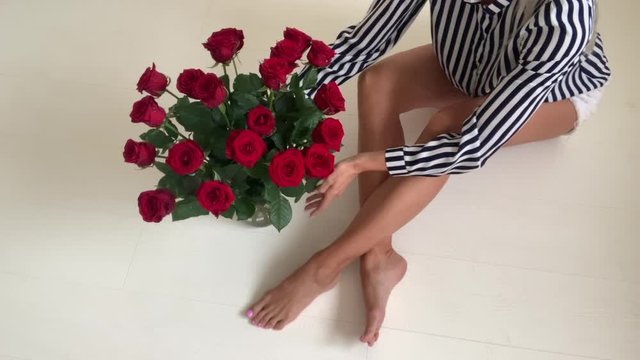 A woman with beautiful long legs sits on the floor and straightens a bouquet of roses