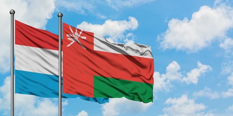 Luxembourg and Oman flag waving in the wind against white cloudy blue sky together. Diplomacy concept, international relations.