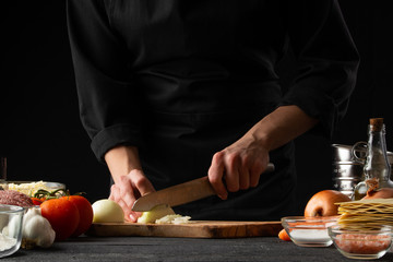 Chef, cook prepares an Italian dish of lasagna, slices onions. Black background. Cooking method. Culinary, gastronomy, restaurant service.