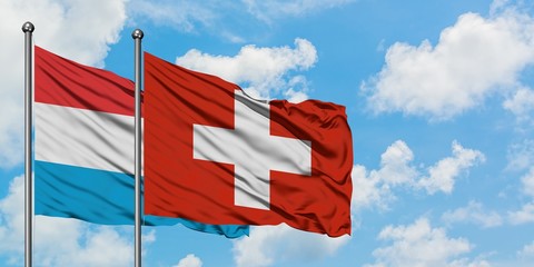 Luxembourg and Switzerland flag waving in the wind against white cloudy blue sky together. Diplomacy concept, international relations.