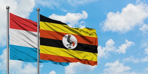 Luxembourg and Uganda flag waving in the wind against white cloudy blue sky together. Diplomacy concept, international relations.