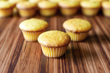 Trio of unfrosted cupcakes on wooden surface.  Additional cupcakes blurred in the background.  Select focus.
