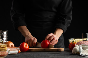 chef, cook prepares Italian lasagna to chop fresh tomatoes to make sauce, dressing. Restaurant business, Italian cuisine, tasty and healthy food