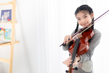 cute asian children holding violin on her shoulder and playing violin in her room, she feeling...