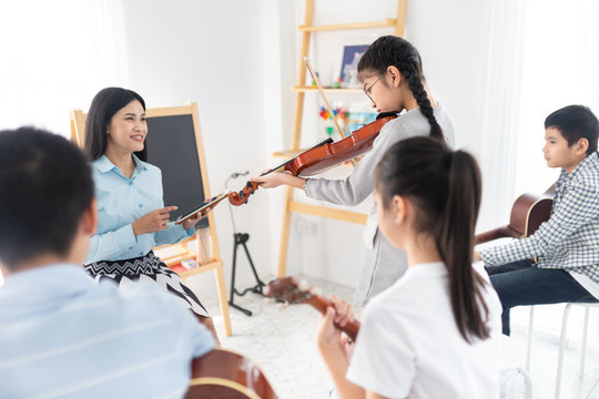 cute asian children holding violin on her shoulder and play violin, she show violin skill and present melody and song to teacher and friends, asian children group in musical training time
