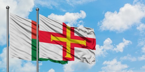 Madagascar and Guernsey flag waving in the wind against white cloudy blue sky together. Diplomacy concept, international relations.