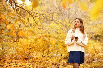 Stylish young woman with cup of coffee in autumn park