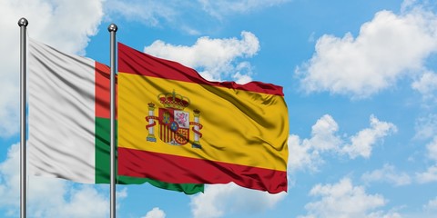 Madagascar and Spain flag waving in the wind against white cloudy blue sky together. Diplomacy concept, international relations.