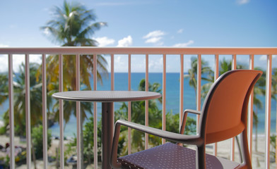 A chair and a table on a balcony with a sunny beach in background
