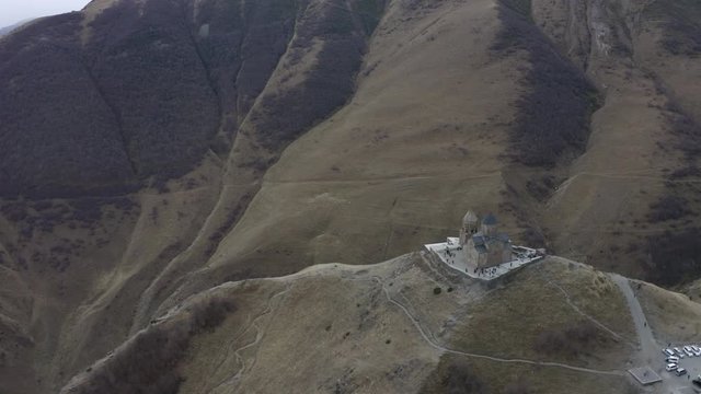 Aerial top landing view ancient georgian church on highland on Kazbek mountain. Old orthodox temple Gergeti Georgia, Stepantsminda on city and mountain valley background
