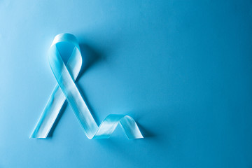 Blue ribbon on bright blue pastel background representing an annual event during the month of...