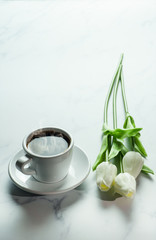 coffee background of a cup of hot black coffee with bunch of white tulip on white marble background