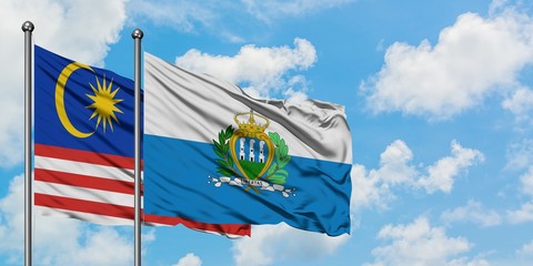 Malaysia and San Marino flag waving in the wind against white cloudy blue sky together. Diplomacy...