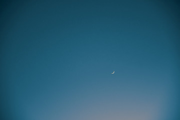 Small crescent moon and a tiny star in a vast evening sky.