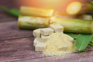 Brown sugar cubes and sugar cane on wooden table and sunlight
