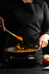 cooking, lasagna, cook prepares dressing, frying in a pan. Black background. Italian-European cuisine. Vertical shot.