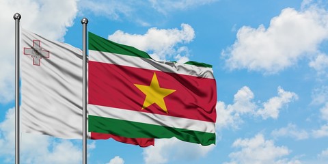 Malta and Suriname flag waving in the wind against white cloudy blue sky together. Diplomacy concept, international relations.