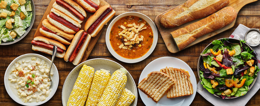 table top meal with hot dogs, grilled cheese, soup and salad in flat lay composition
