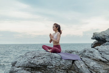 Fototapeta na wymiar Side view of woman doing exercise yoga. sitting in Sukhasana exercise, Easy Seat pose pose. Amazing yoga landscape in beautiful and enjoying sea view with evening, concept for exercising, health care