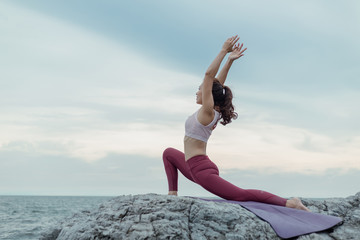 Young woman doing yoga exercise yoga master pose on the rock. Amazing yoga landscape in beautiful sky and enjoying sea view on wooden floor, concept for exercising, health care