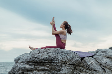 Young woman doing yoga exercise yoga master pose on the rock. Amazing yoga landscape in beautiful...