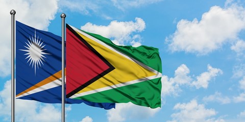 Marshall Islands and Guyana flag waving in the wind against white cloudy blue sky together. Diplomacy concept, international relations.