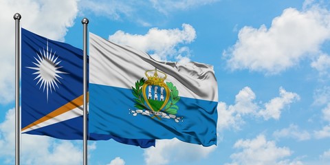 Marshall Islands and San Marino flag waving in the wind against white cloudy blue sky together....