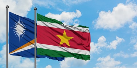 Marshall Islands and Suriname flag waving in the wind against white cloudy blue sky together. Diplomacy concept, international relations.