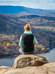 Teenage girl sits on the cliff of Breakneck Ridge trail - obrazy, fototapety, plakaty