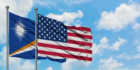 Marshall Islands and United States flag waving in the wind against white cloudy blue sky together. Diplomacy concept, international relations.
