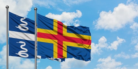Martinique and Aland Islands flag waving in the wind against white cloudy blue sky together. Diplomacy concept, international relations.