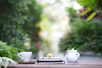 White cup and flower with white tea pot and notebooks on wooden table