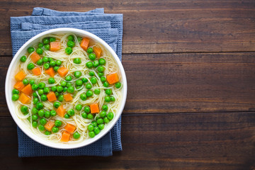 Fresh homemade vegetable noodle soup with carrot, peas, onion and angel hair pasta in white soup bowl, photographed overhead with copy space on the right side